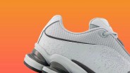 Close-up of a white and gray sneaker with mesh and textured leather upper against an orange background.
