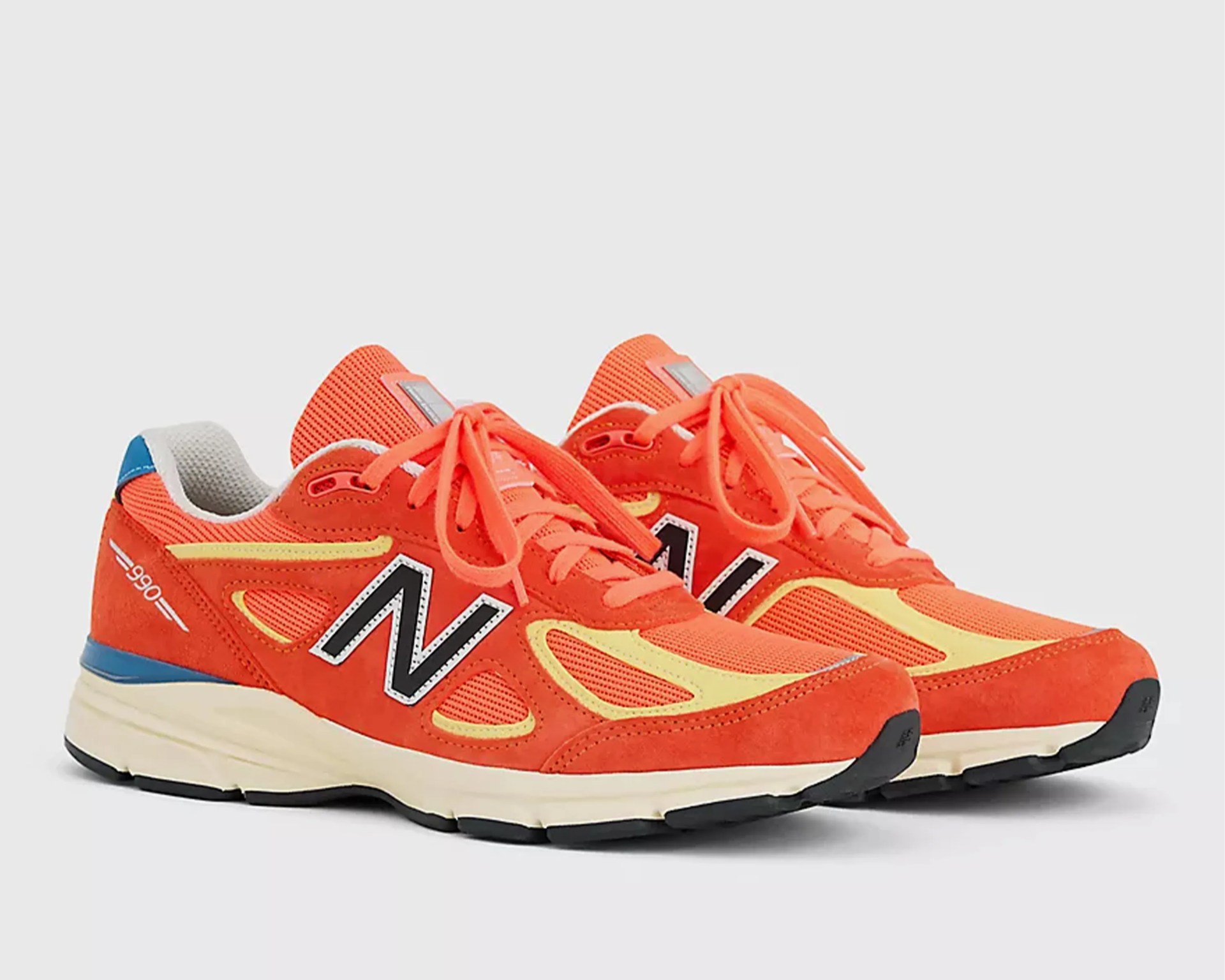 Pair of orange New Balance 990 sneakers with yellow accents and black soles.