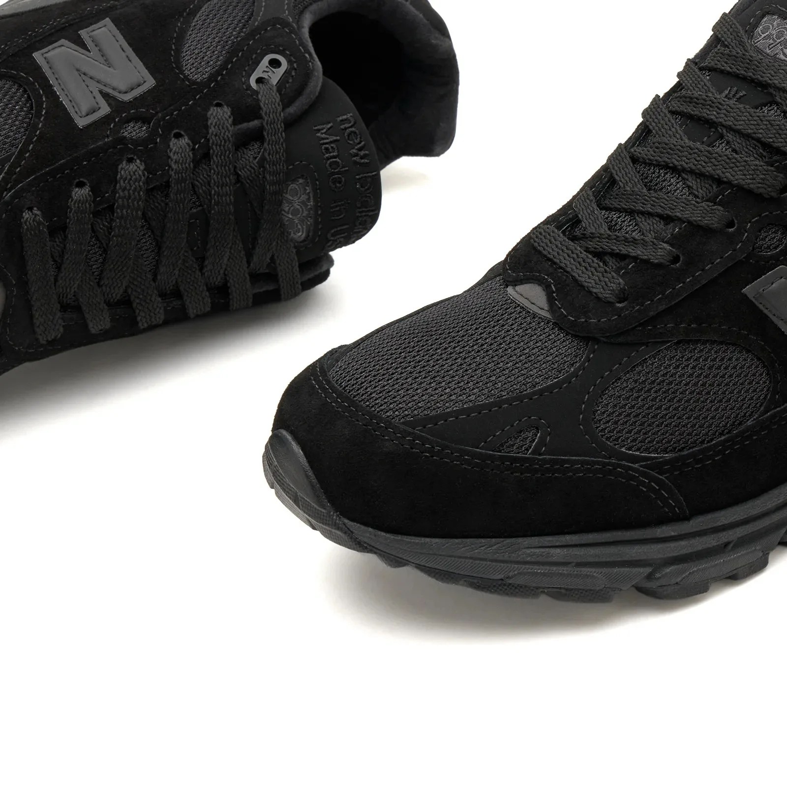 Pair of black New Balance sneakers with suede and mesh panels and black laces on a white background.