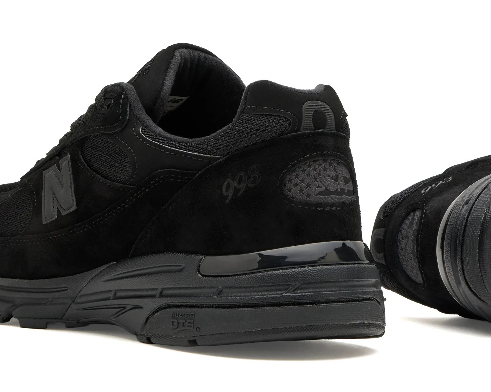 Pair of black New Balance 993 sneakers with suede and mesh upper and USA flag detail on heel.