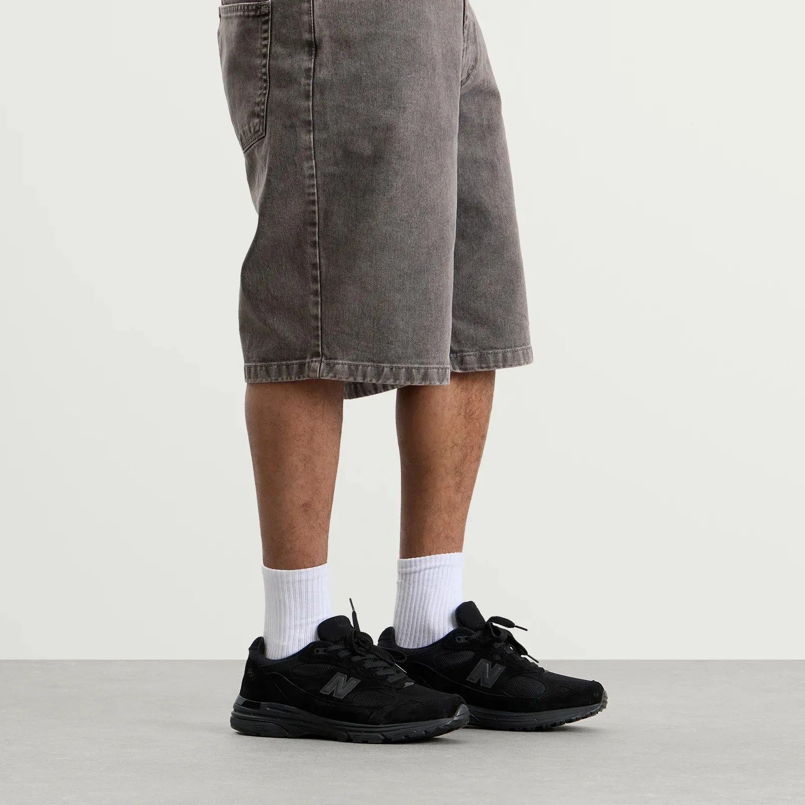 Gray denim shorts worn with white socks and black New Balance sneakers on a gray floor.
