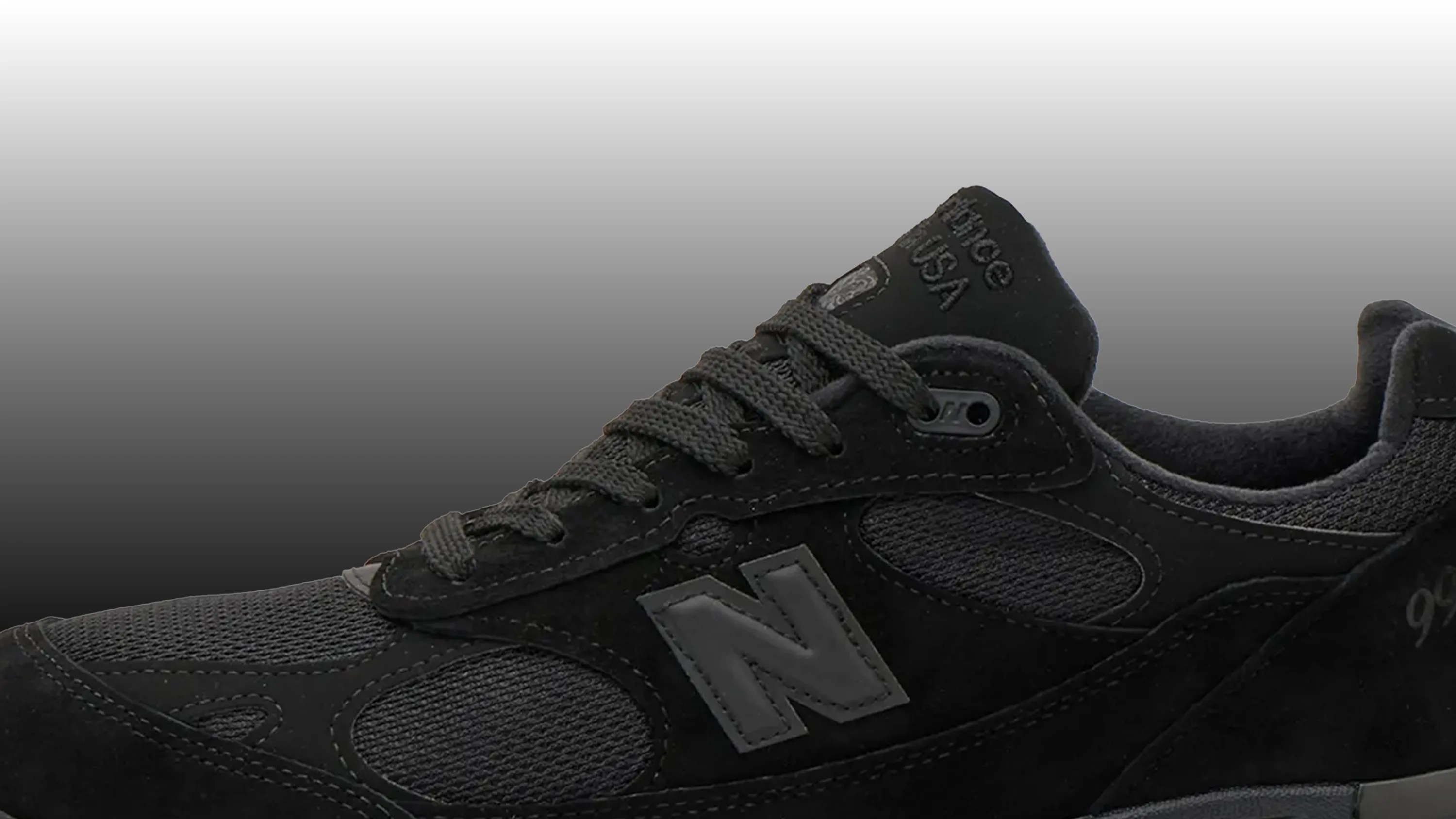 Close-up of a black New Balance sneaker with mesh and suede panels and gray "N" logo on the side.