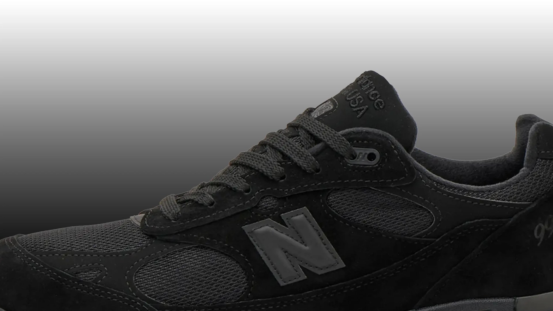 Close-up of a black New Balance sneaker with mesh and suede panels and gray "N" logo on the side.