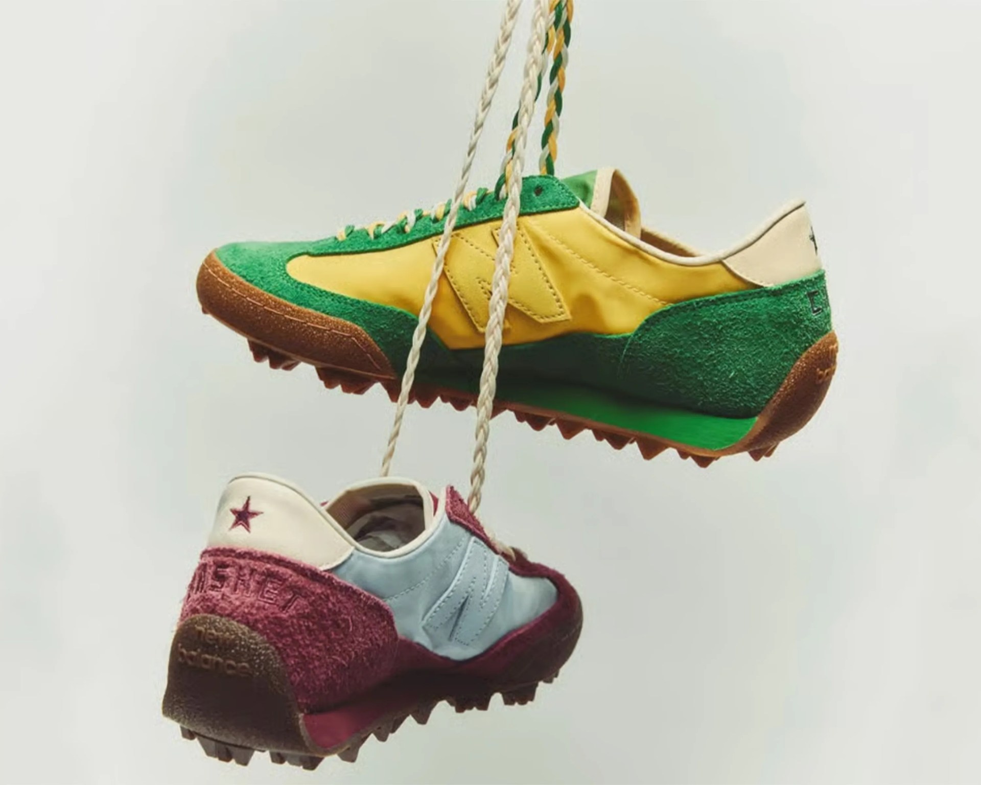 Two hanging New Balance sneakers, one green and yellow with brown sole, the other white and burgundy with textured heel.