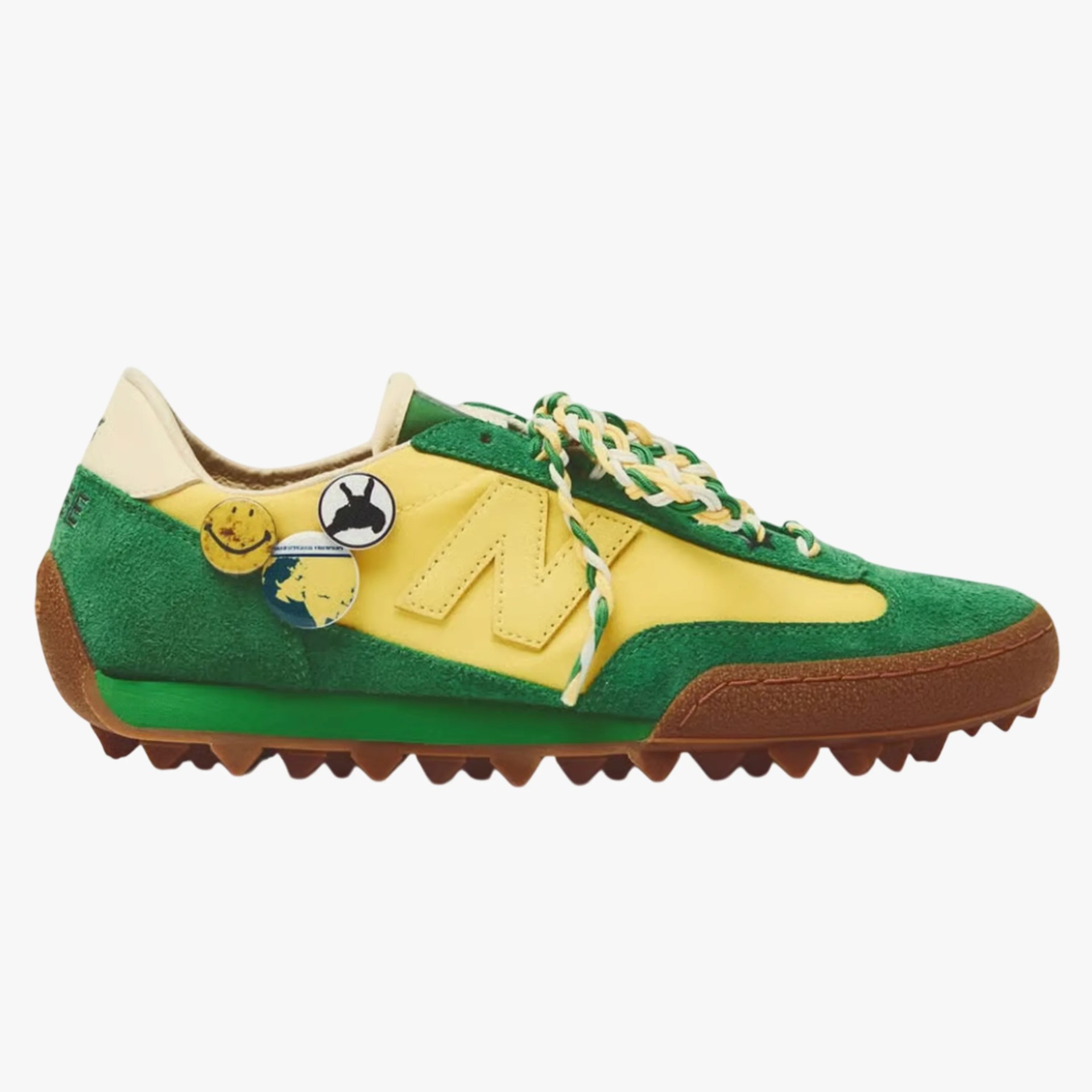 Green and yellow suede sneaker with braided laces and decorative pins on the side.