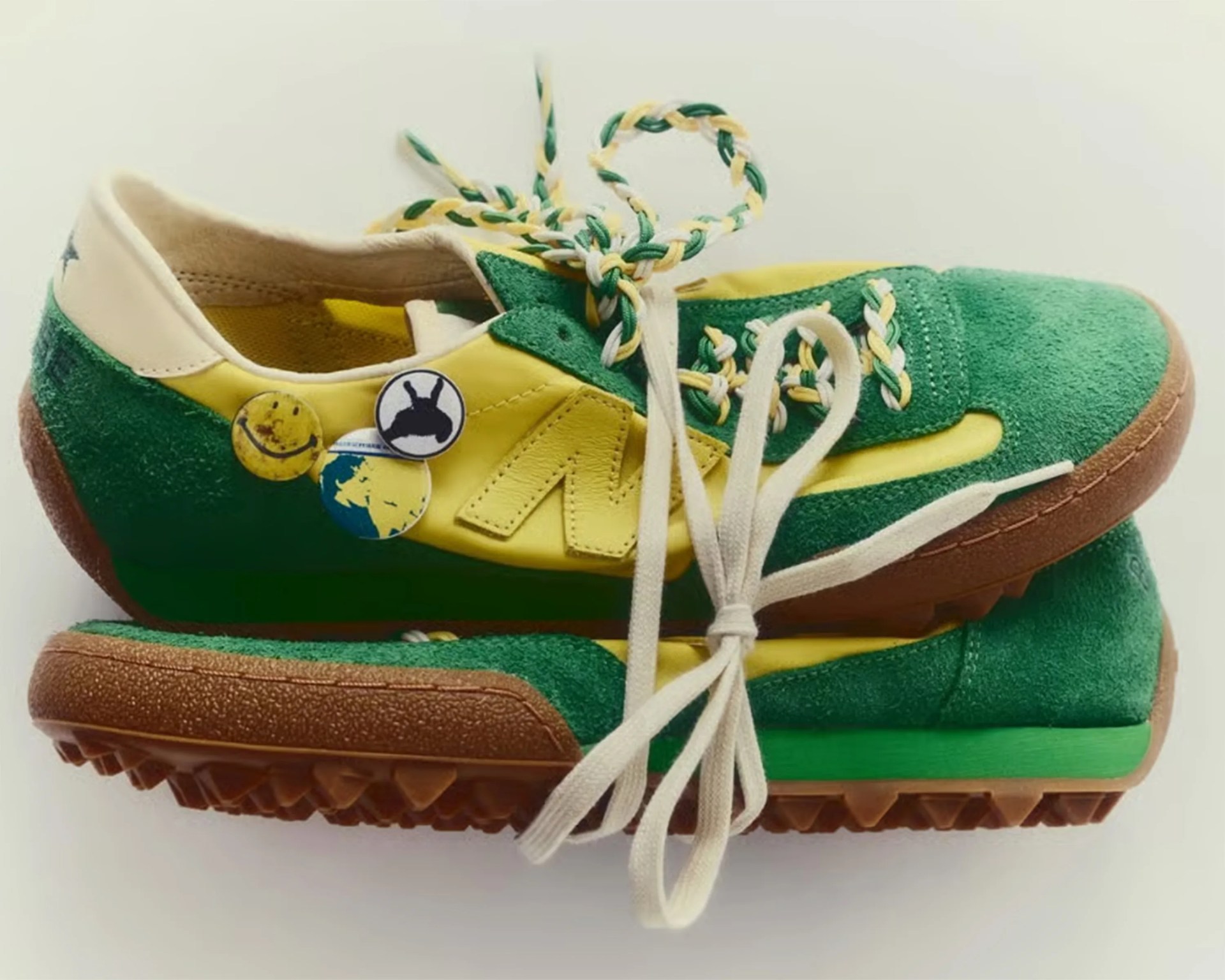 Green and yellow suede sneakers with brown textured soles and multicolored braided laces.