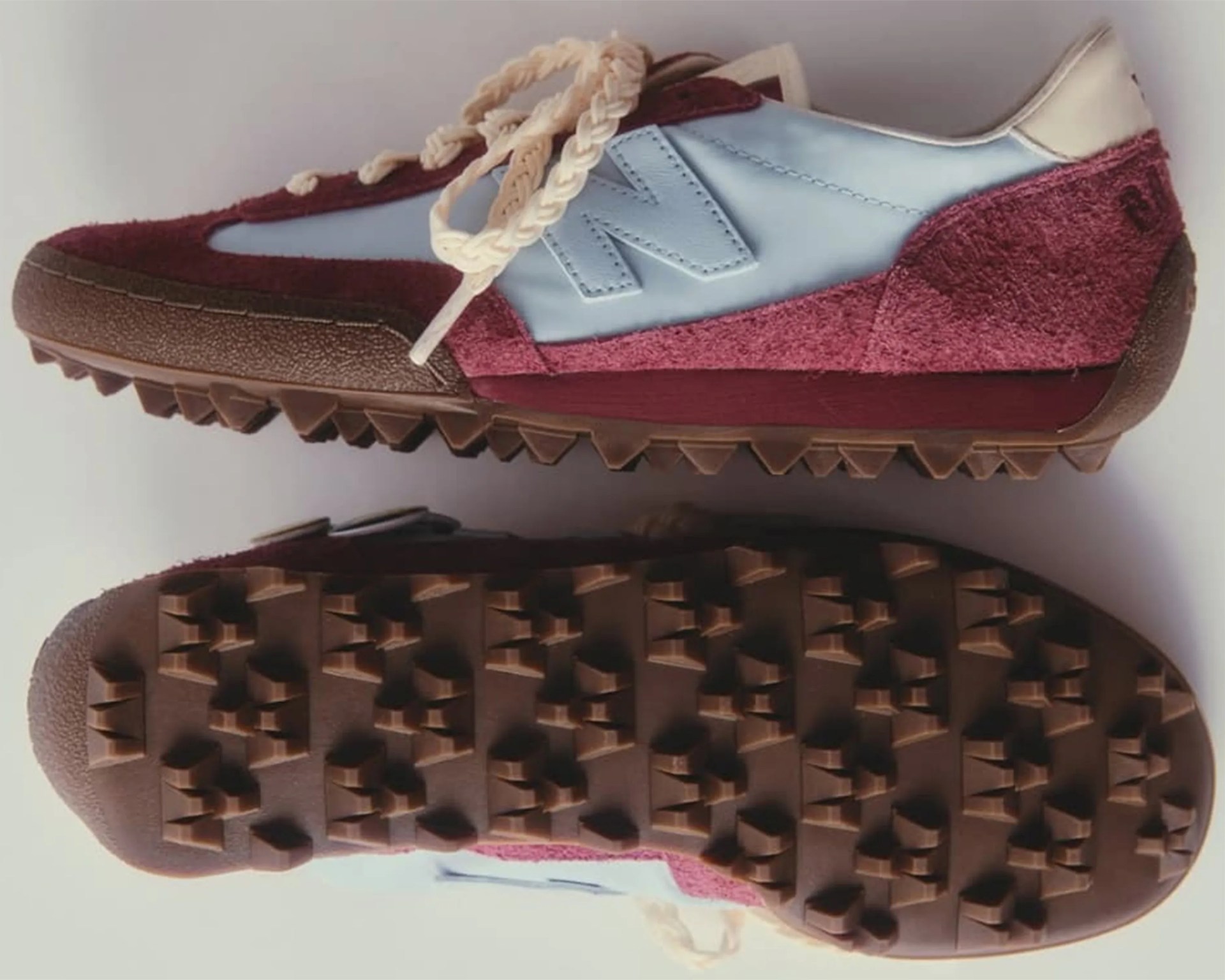 Light blue and maroon New Balance sneaker with cream braided laces and brown textured sole.