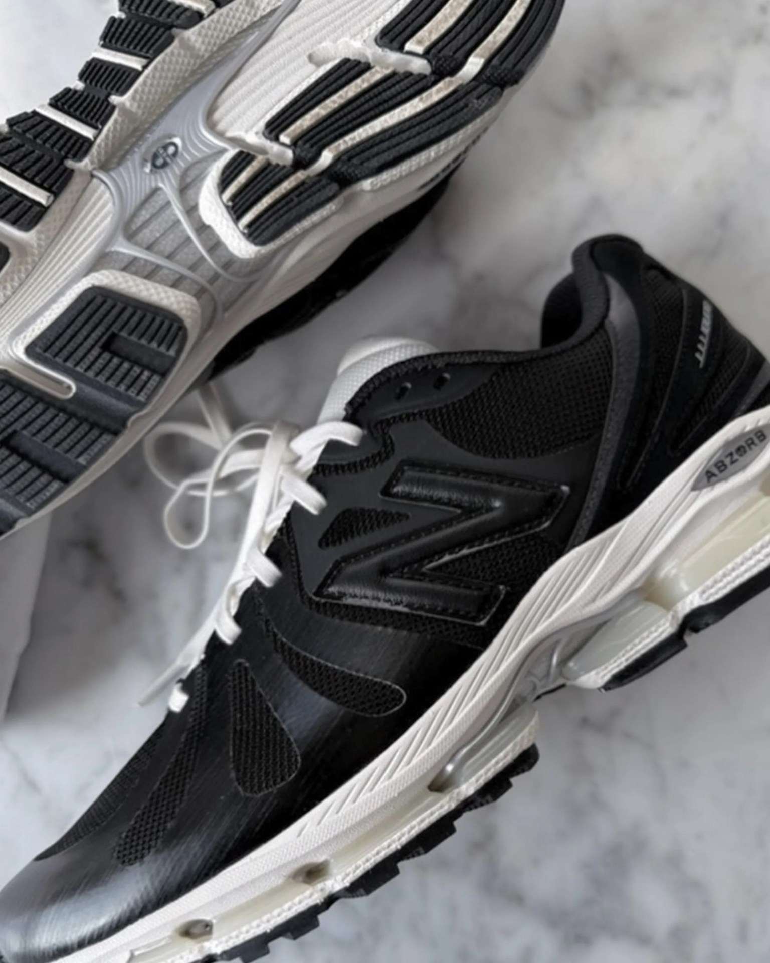 Black and white New Balance running shoes with mesh upper and ABZORB cushioning on a marble surface.