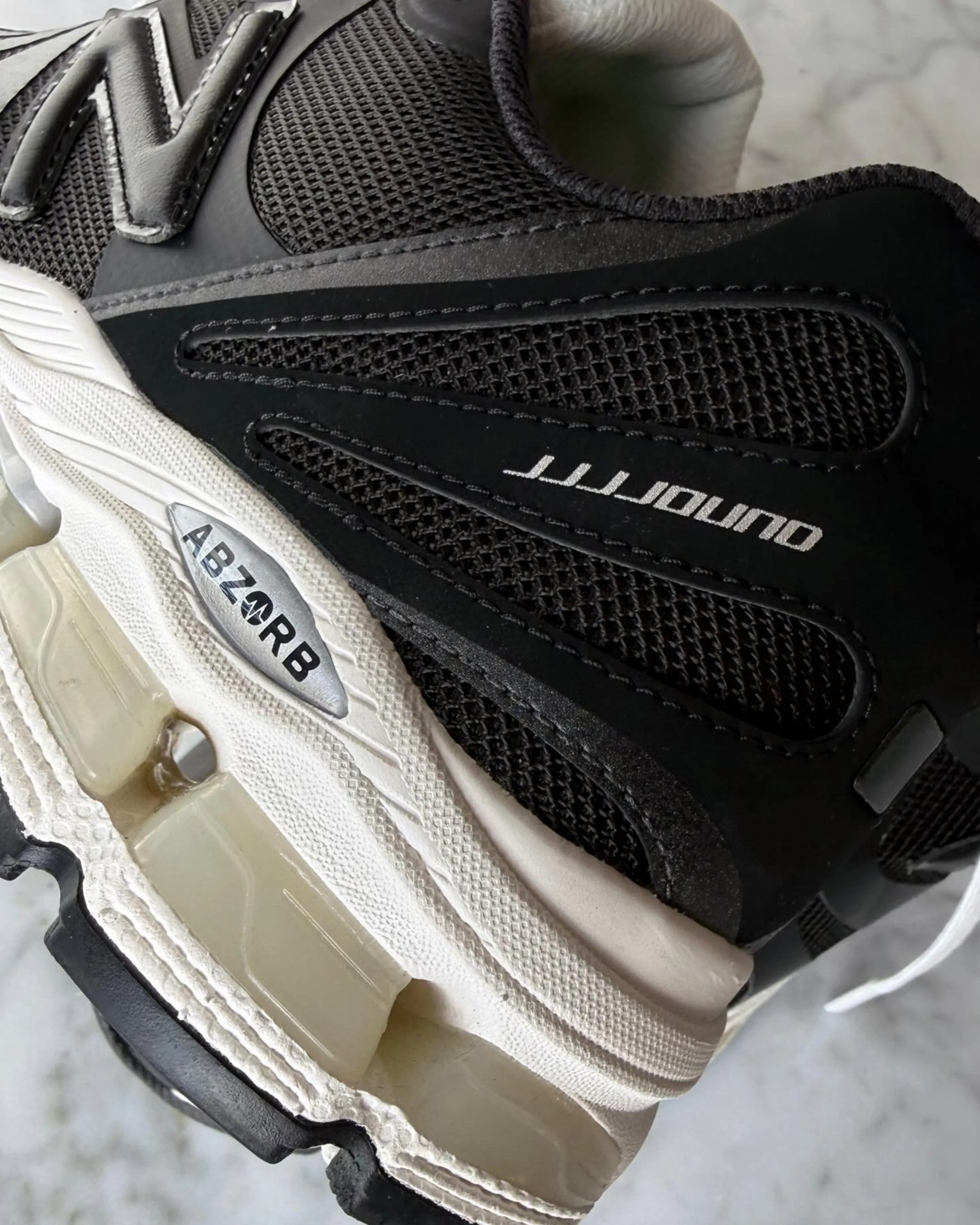 Close-up of black and gray New Balance sneaker with mesh upper and white sole featuring ABZORB cushioning.