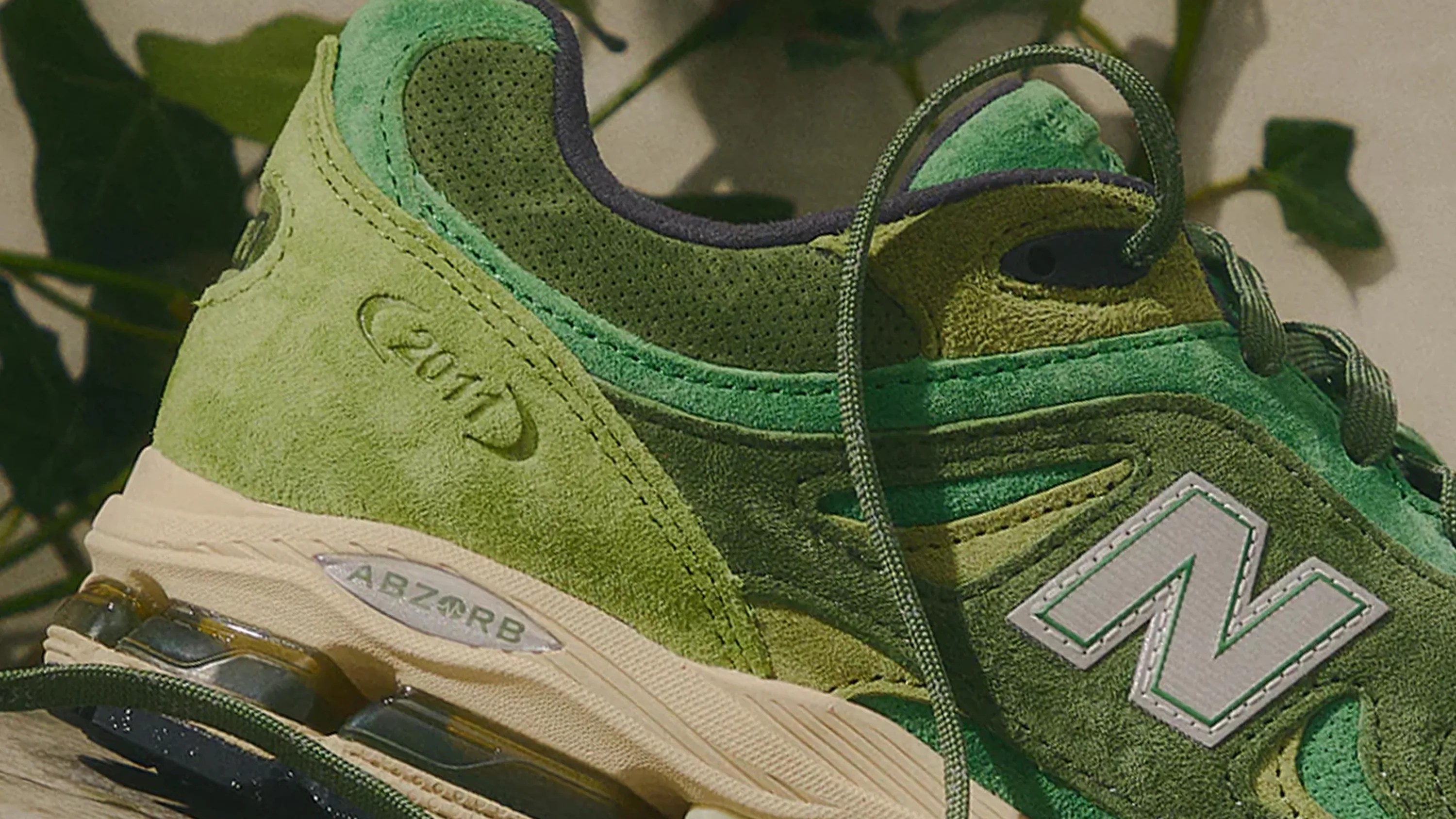 Green suede New Balance sneaker with ABZORB cushioning and "2011" embossed on the heel.