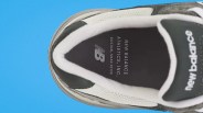 Top view of a New Balance sneaker with black insole and white padded collar on a blue background.