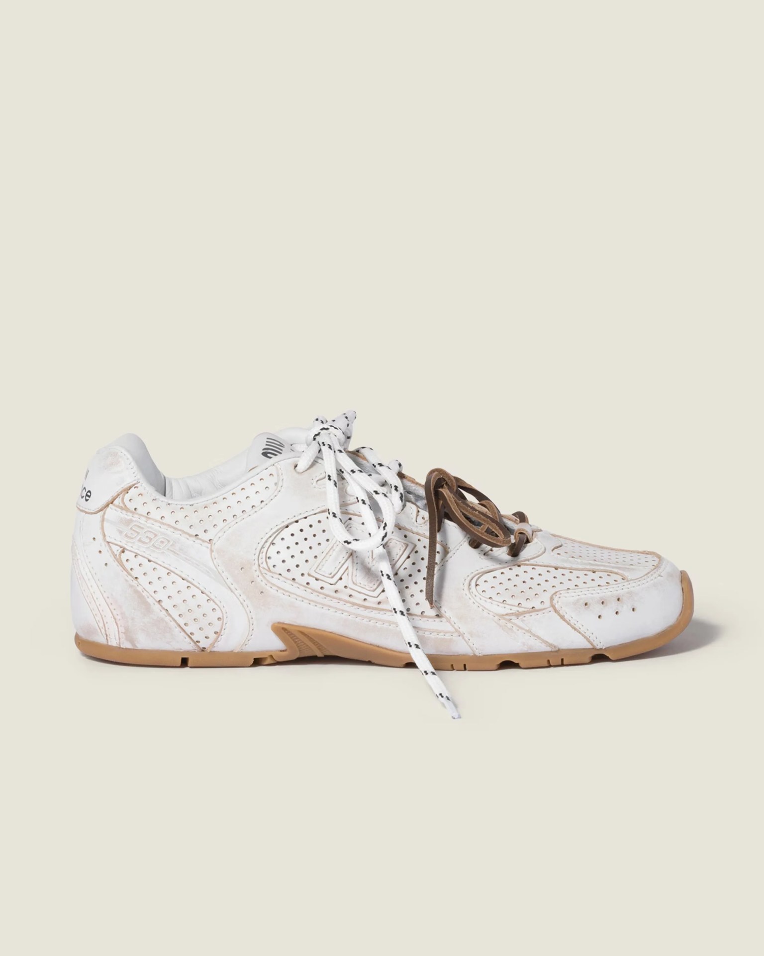 White perforated leather sneaker with gum sole and mismatched white and brown laces.