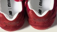 Pair of red suede New Balance sneakers showing the heel and white inner lining with logo on the insole.