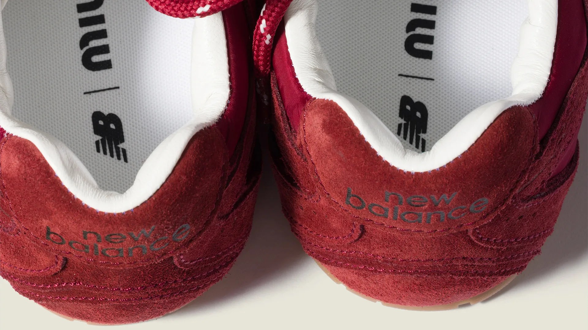 Pair of red suede New Balance sneakers showing the heel and white inner lining with logo on the insole.