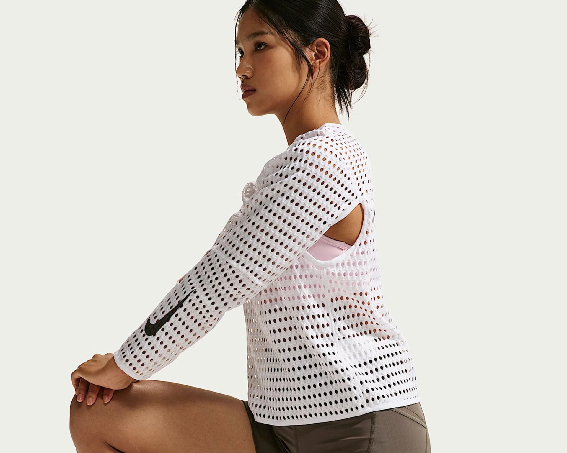 Woman wearing a white perforated long-sleeve top with a black Nike swoosh on the sleeve and olive shorts.