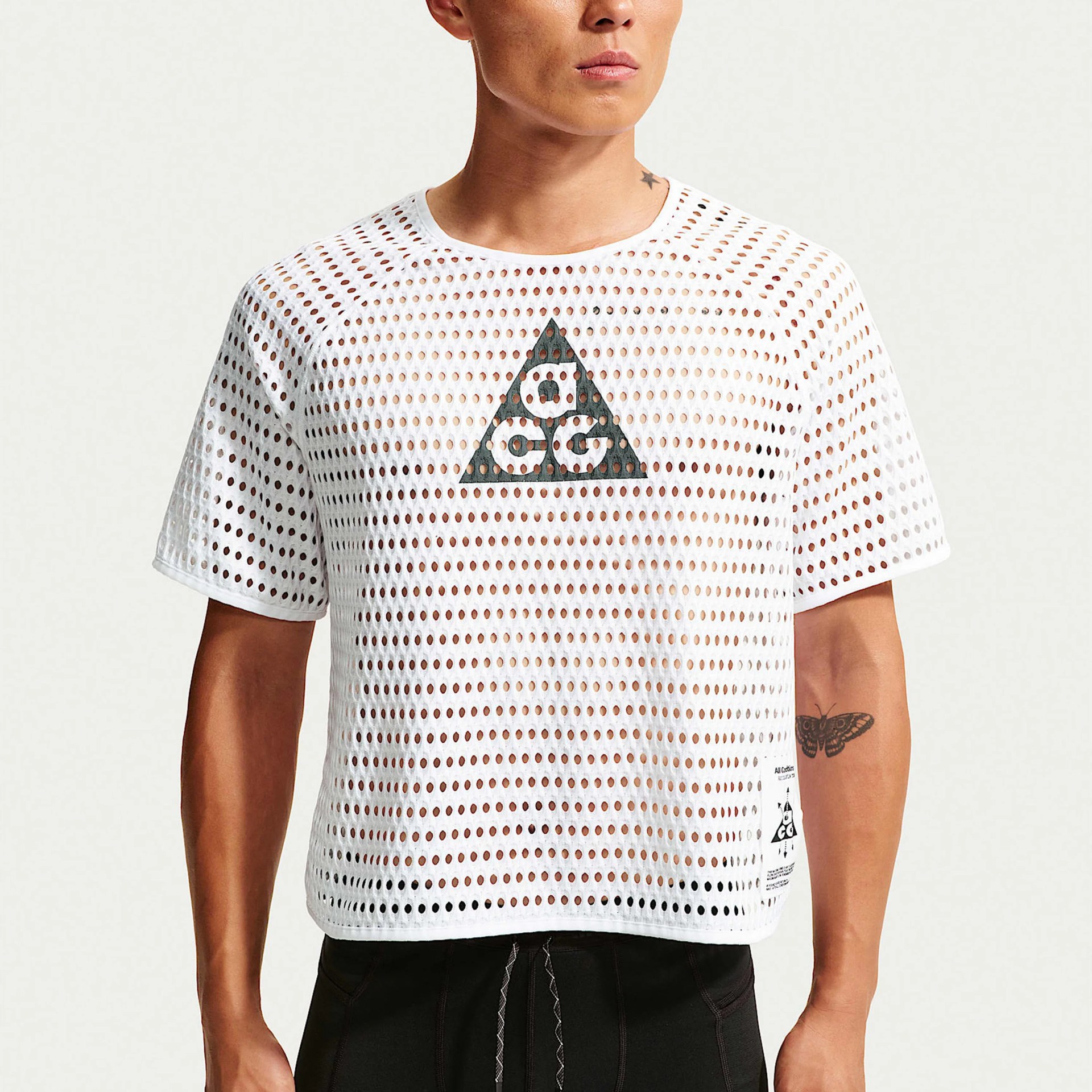 White perforated short-sleeve shirt with black triangular logo on chest worn by a person.