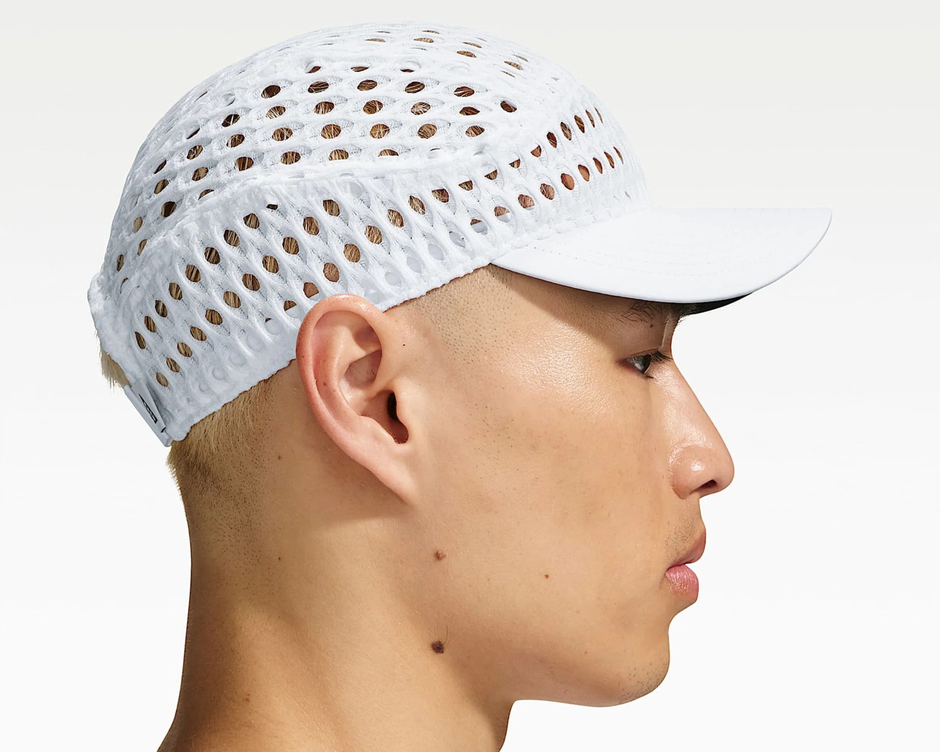 White mesh cap with large ventilation holes worn on a person's head, showing side profile.