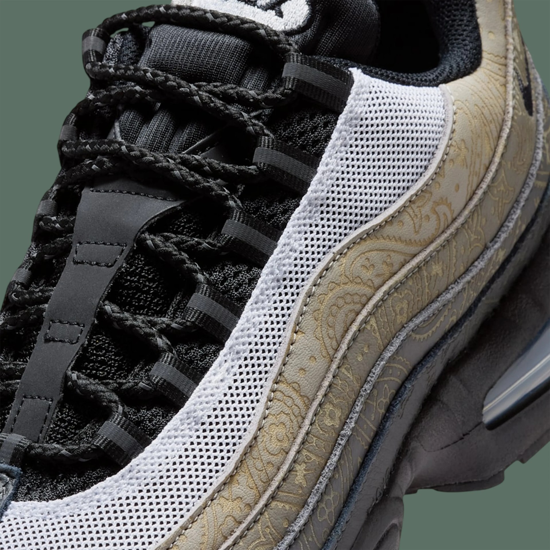 Close-up of a black sneaker with braided black laces, white mesh panel, and beige paisley-patterned leather detail.