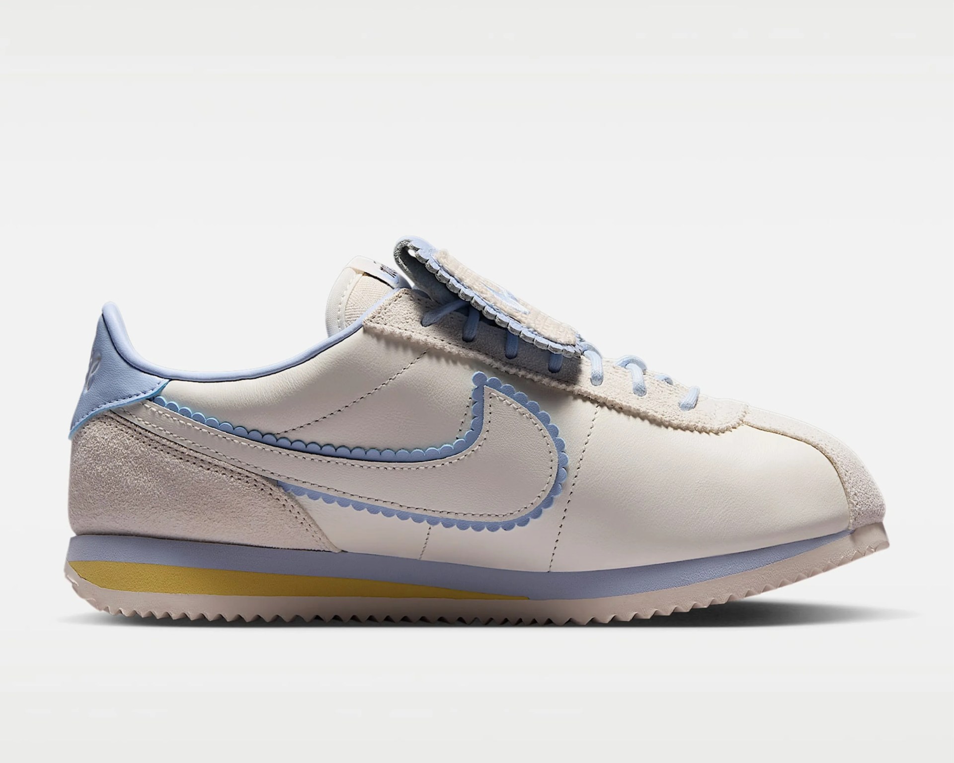 Off-white and light blue Nike sneaker with scalloped edges and a yellow stripe on the sole.