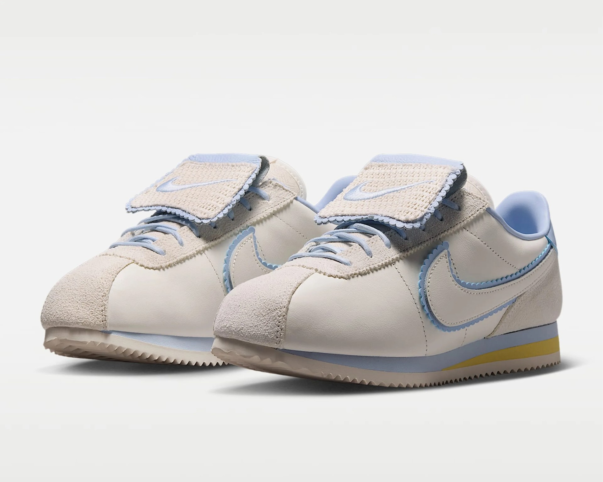 Pair of cream and light blue Nike sneakers with woven tongue flaps and yellow accents on the sole.
