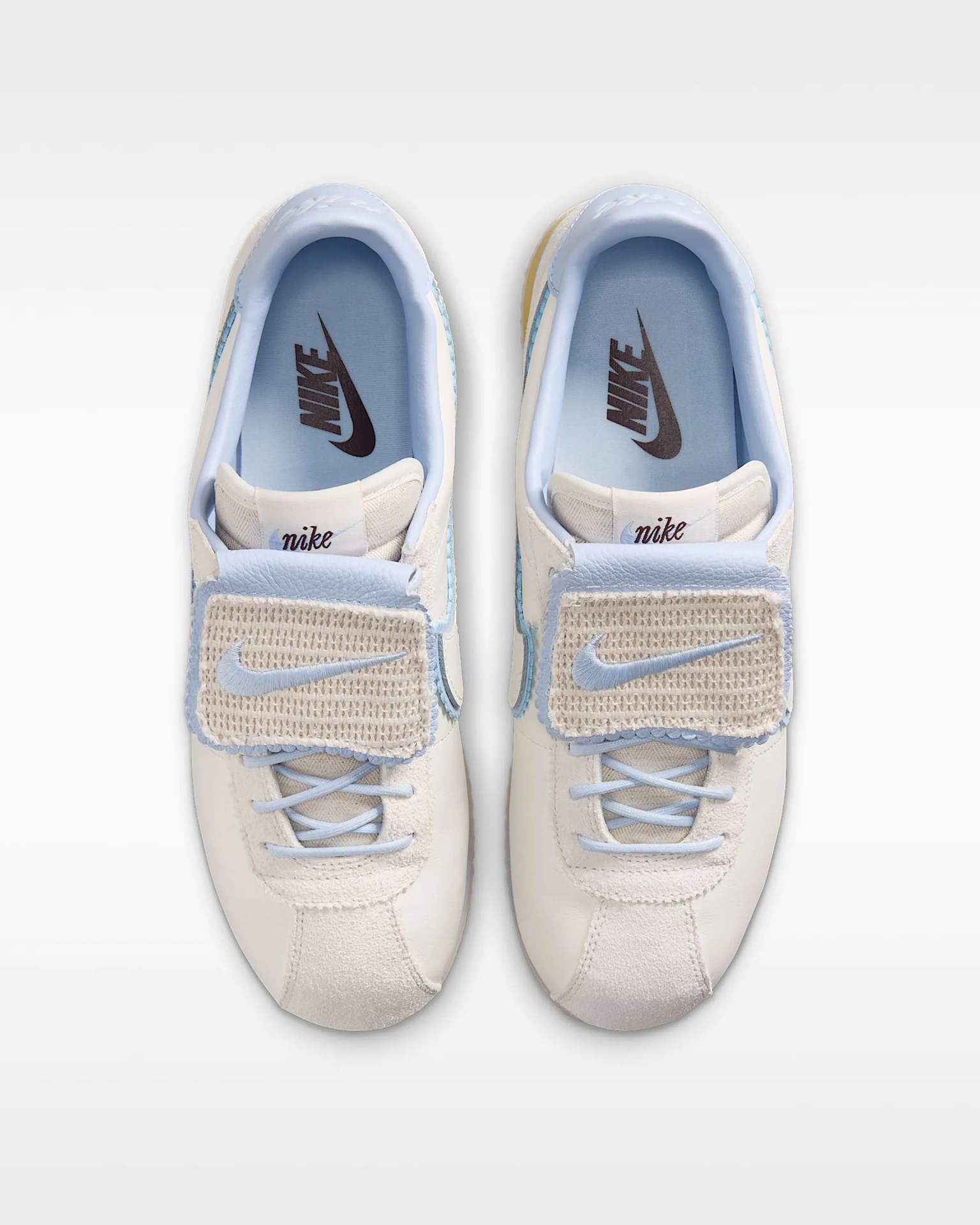 Pair of white and light blue Nike sneakers with woven velcro straps and black Nike logos on light blue insoles.