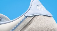 Close-up of a white and light blue sneaker heel with suede and leather textures against a blue background.