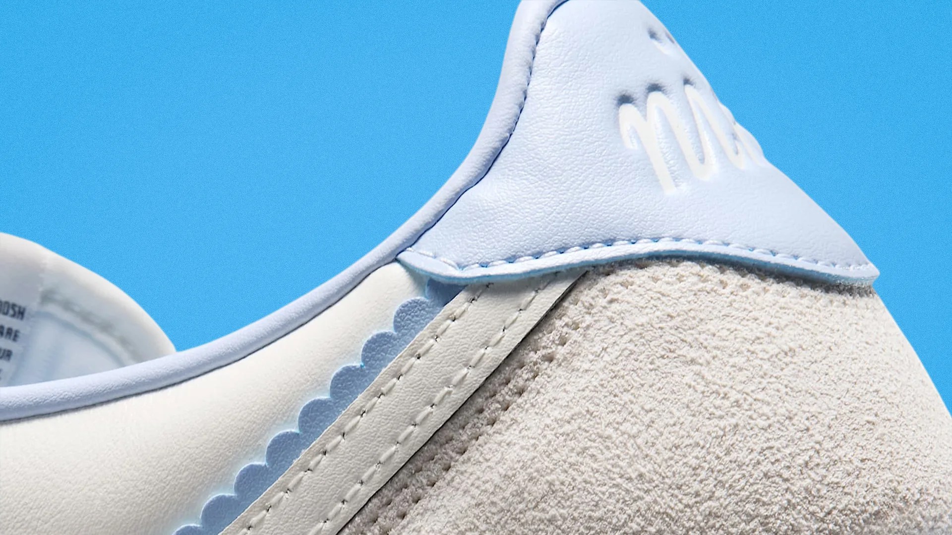 Close-up of a white and light blue sneaker heel with suede and leather textures against a blue background.