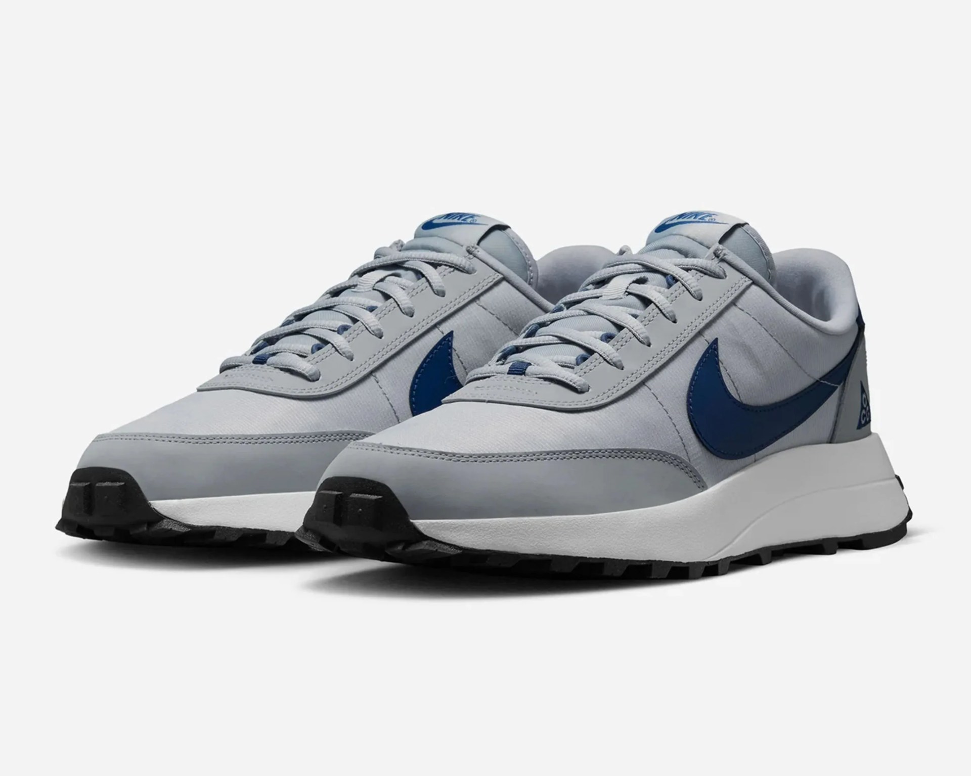 Pair of light gray Nike sneakers with dark blue swoosh logos and black rubber soles.