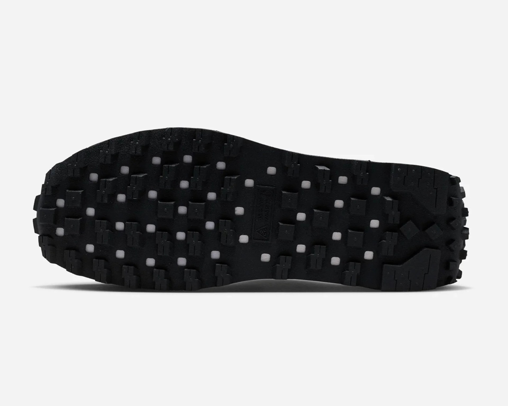 Black rubber shoe sole with square and rectangular tread patterns and small white inserts.