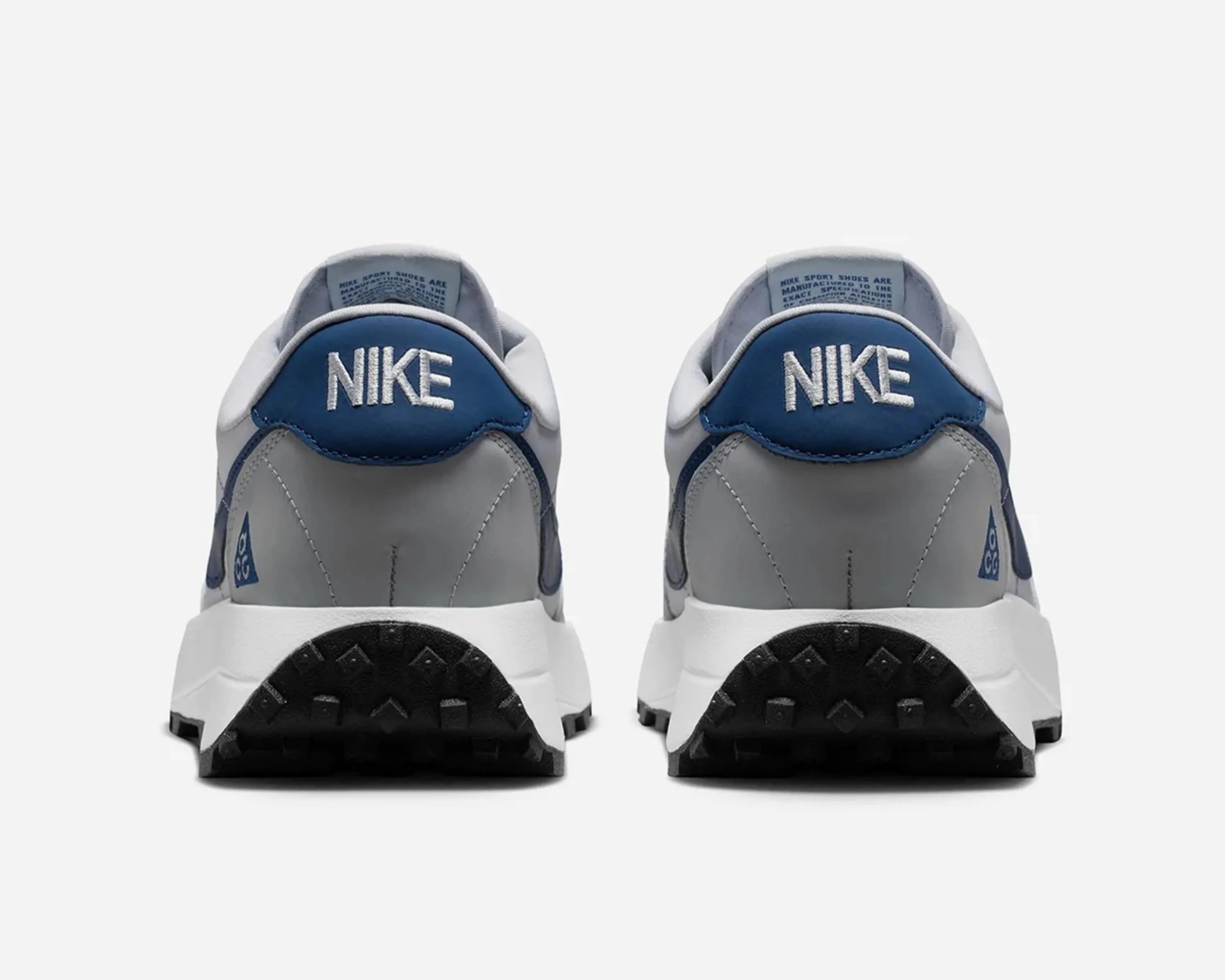Pair of gray and blue Nike sneakers viewed from the back showing the "NIKE" logo on the heel tab and black outsole.