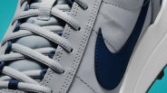 Close-up of light gray sneaker with blue Nike swoosh and matching laces on a teal background.