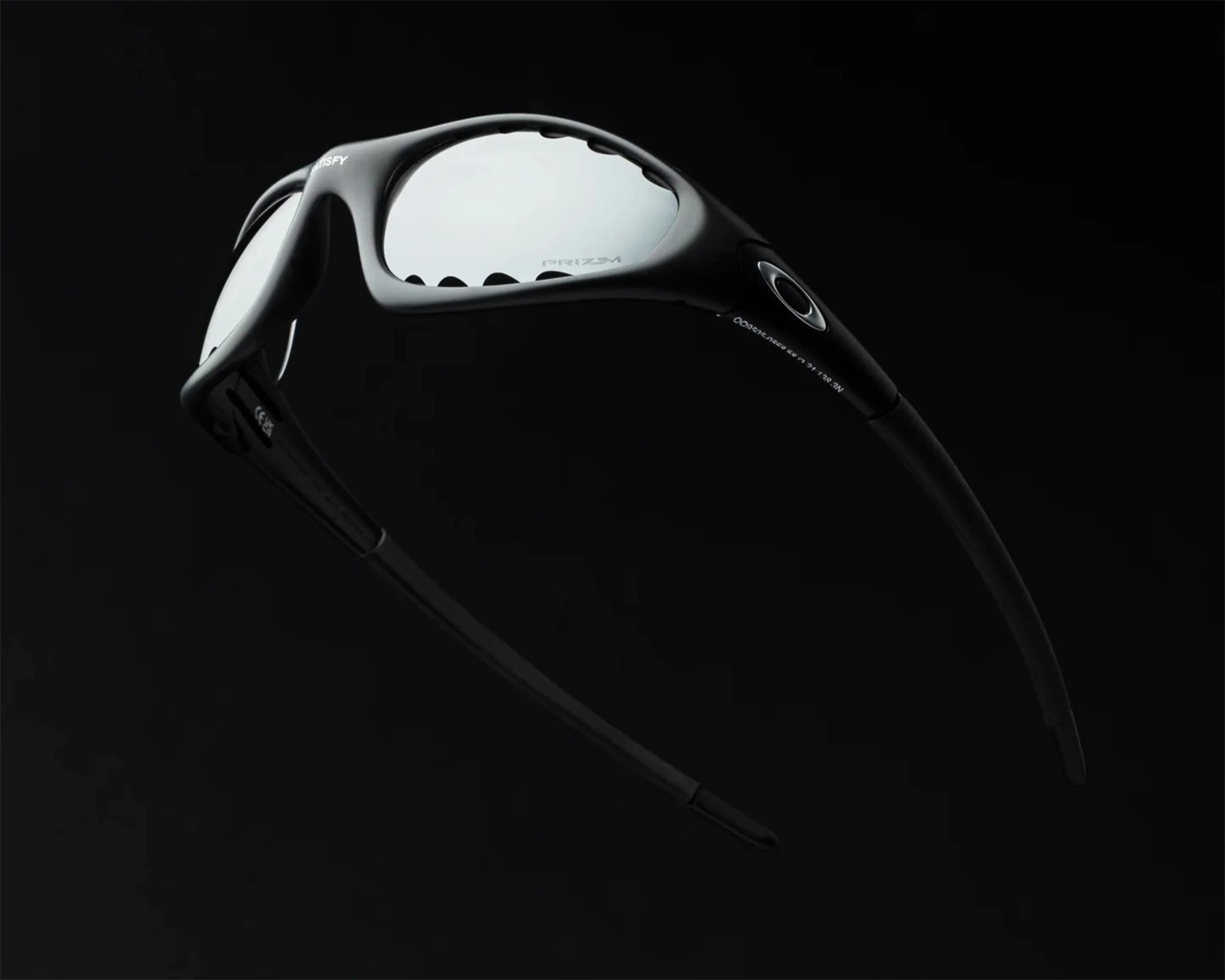 Black Oakley sunglasses with reflective Prizm lenses and a matte finish frame against a black background.