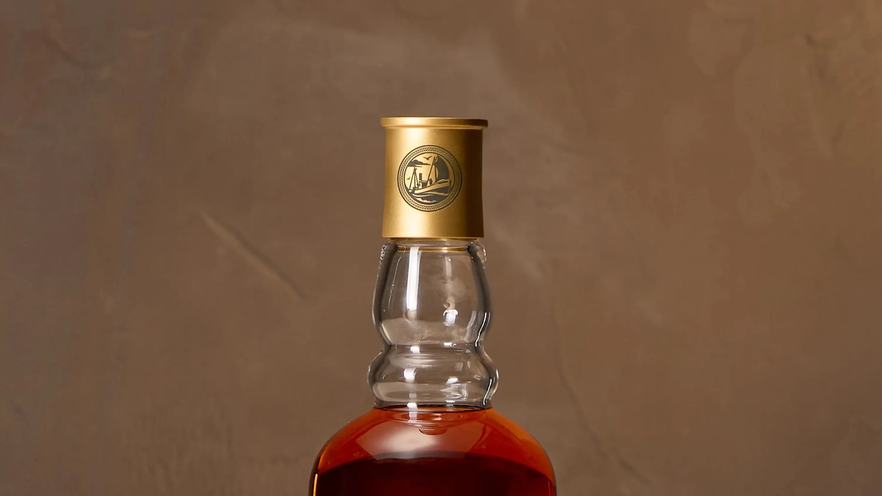 Close-up of a bottle neck with a gold cap featuring a black emblem of a ship and waves.