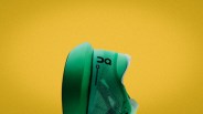 Green athletic shoe with black "On" logo on the side against a yellow background.