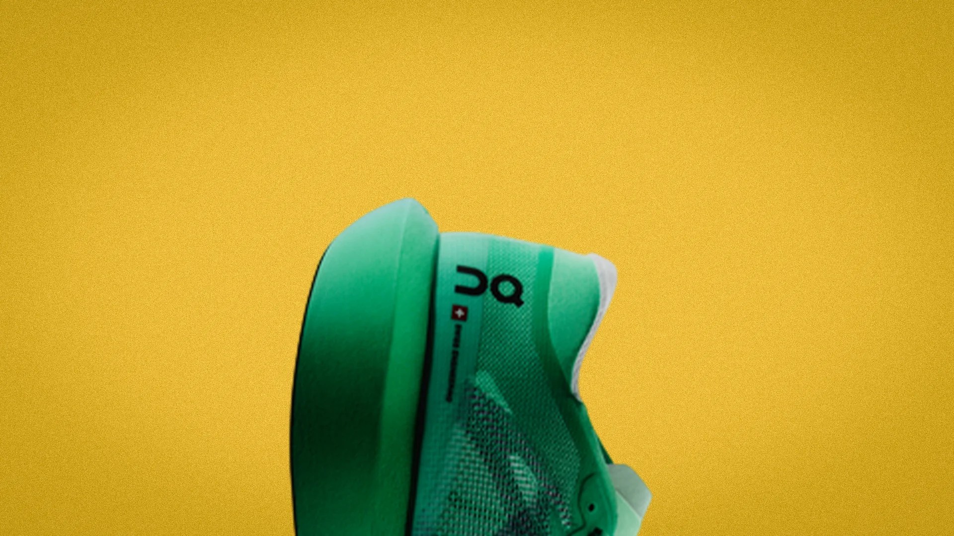 Green athletic shoe with black "On" logo on the side against a yellow background.