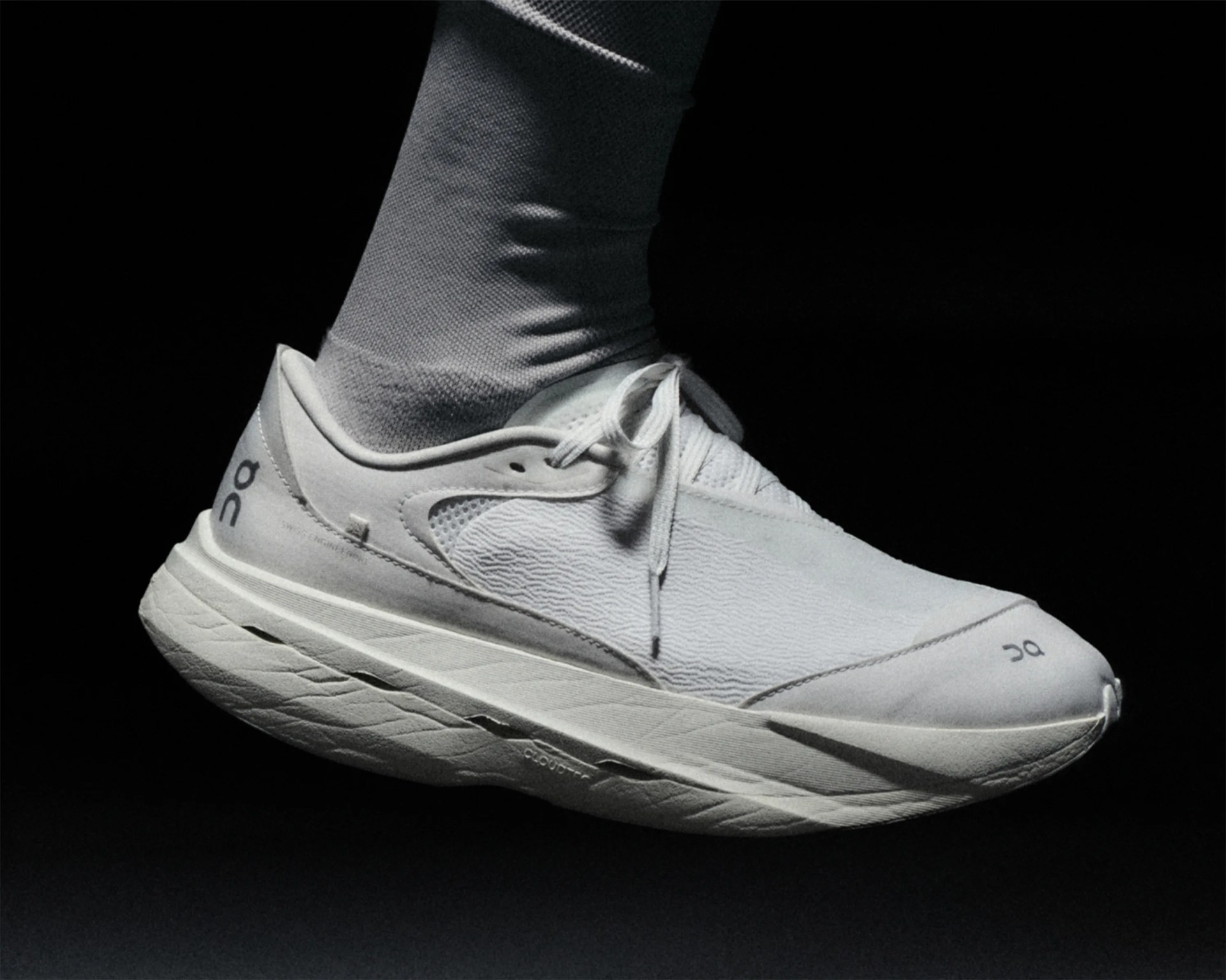 White On running shoe with textured upper and cushioned sole worn with white sock against black background.