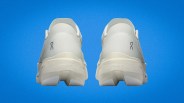 Pair of off-white On running shoes viewed from the back against a blue background.