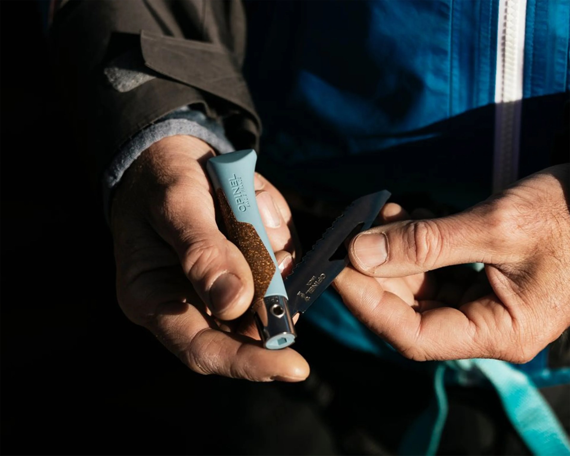 Hands holding a blue and brown Opinel folding knife with a serrated blade.