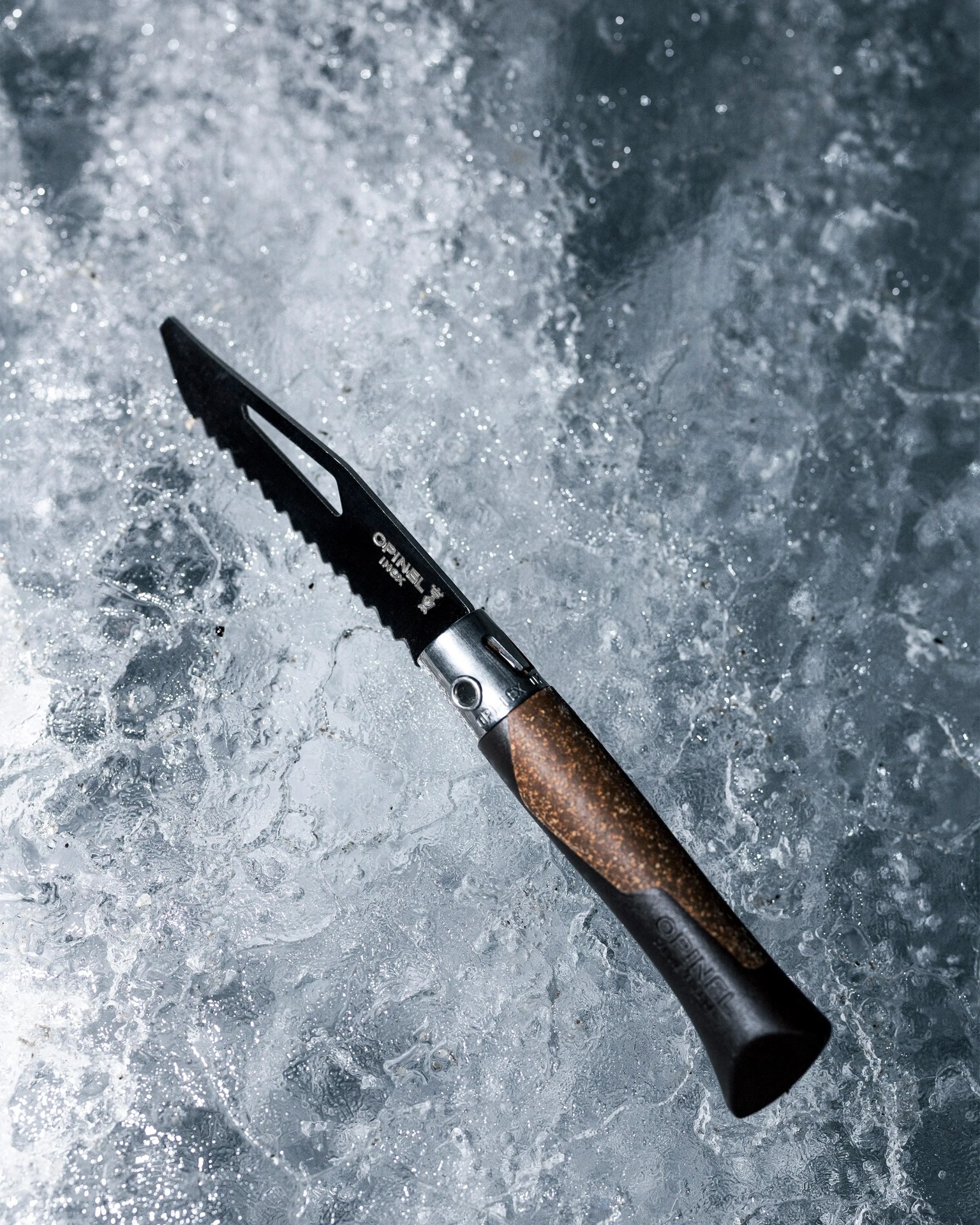 Serrated Opinel folding knife with wooden handle on textured icy surface.