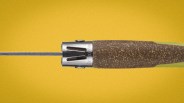 Close-up of a knife handle with a cork grip and a metal bolster on a yellow background.
