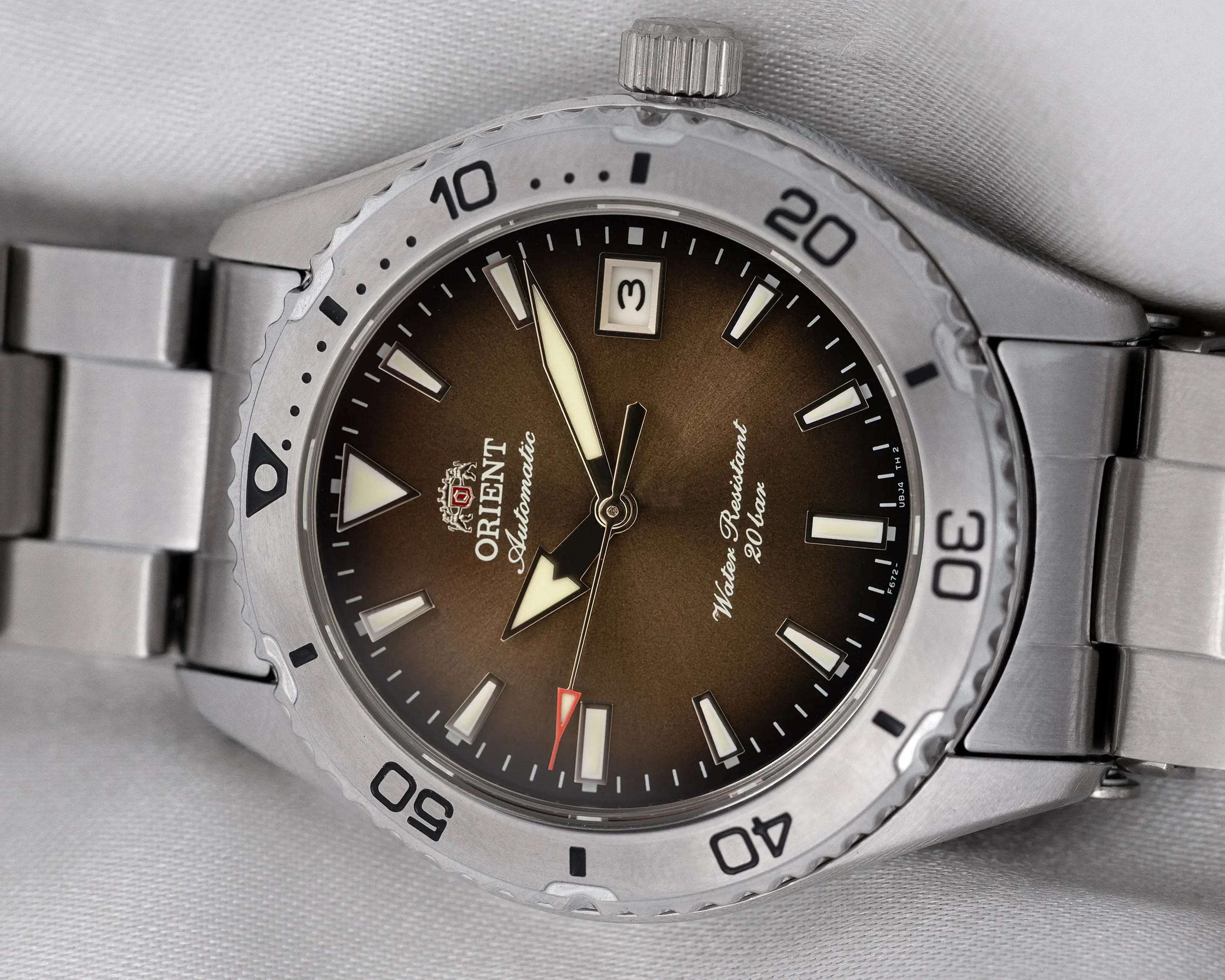 Close-up of a stainless steel Orient automatic watch with a brown gradient dial and date window at 3 o'clock.