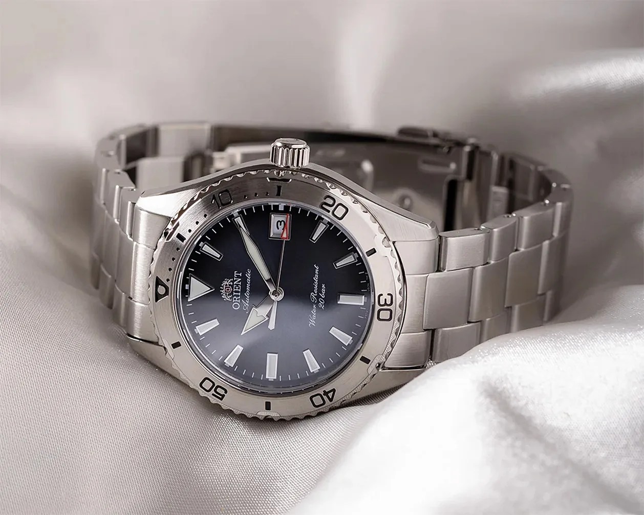 Silver stainless steel Orient automatic wristwatch with black dial and date display on white fabric.