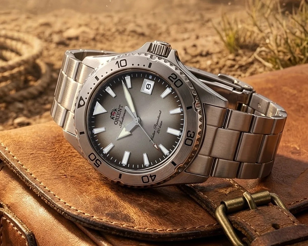 Silver stainless steel Orient automatic wristwatch with gray gradient dial and date window, resting on a brown leather bag.