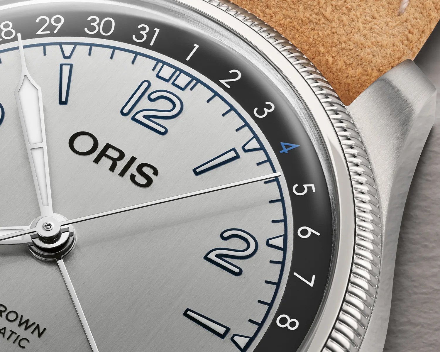 Close-up of an Oris watch dial with silver hands, blue and black date ring, and a tan leather strap.