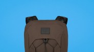 Brown Osprey backpack with black adjustable straps and front bungee cord on blue background.