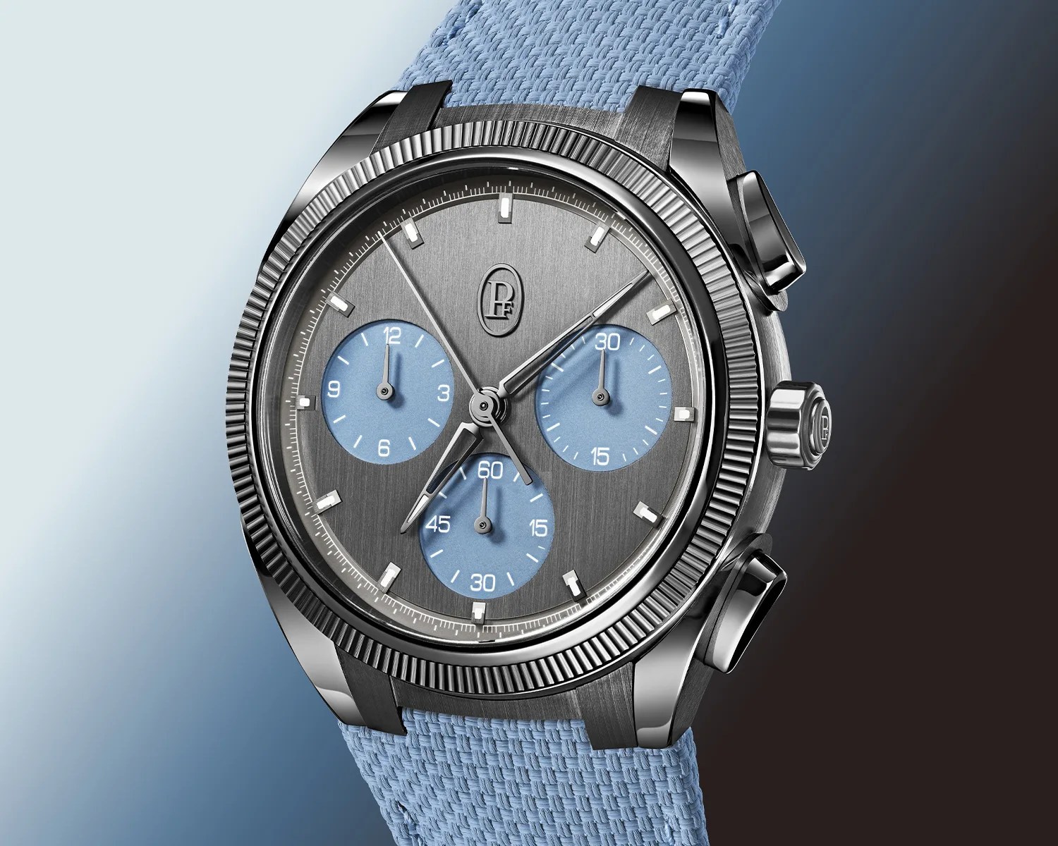Chronograph wristwatch with a brushed gray dial, three blue subdials, and a light blue woven strap.