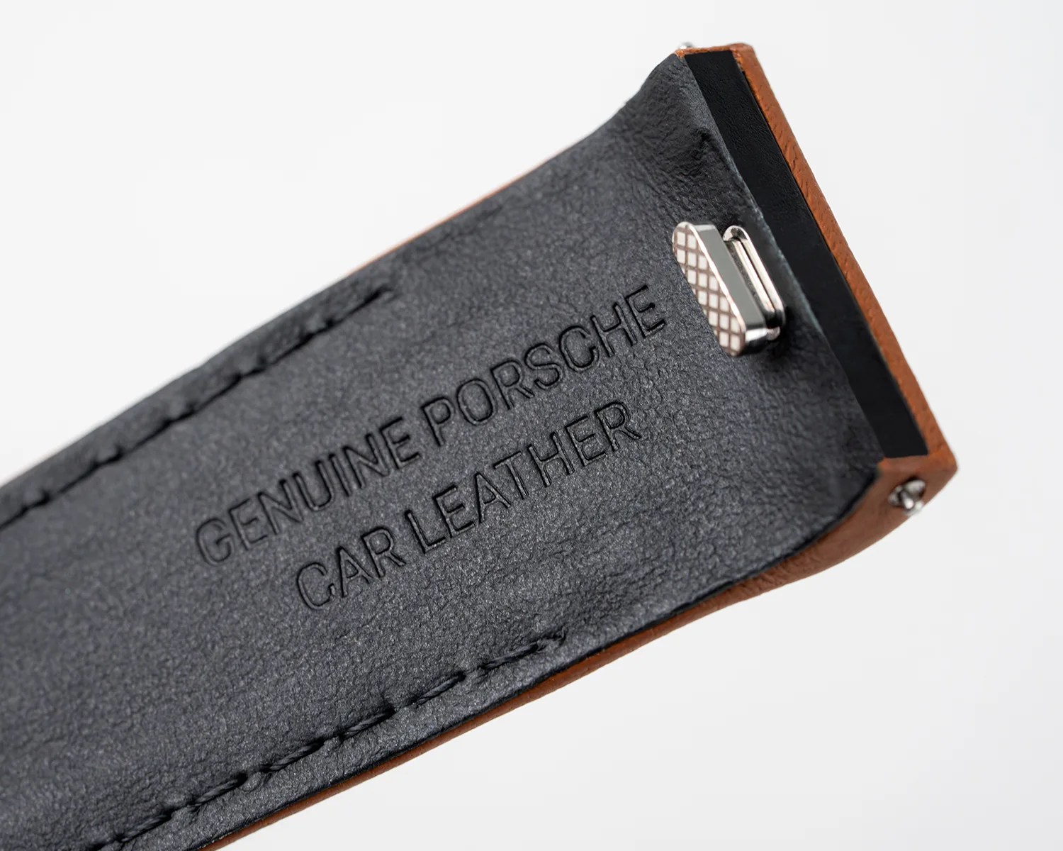 Close-up of black genuine Porsche car leather strap with brown edges and metal clip.
