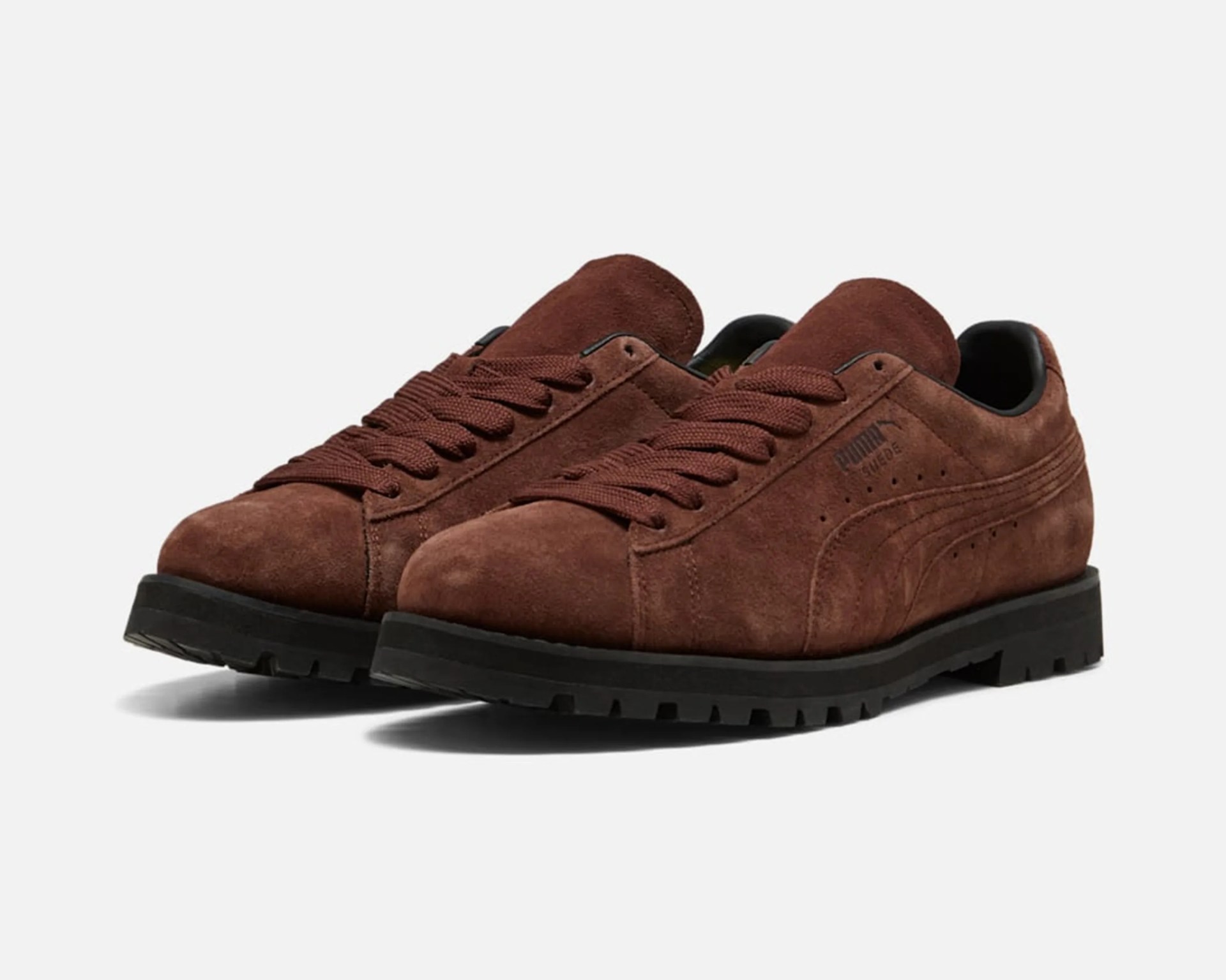 Brown suede Puma sneakers with thick black rubber soles and matching brown laces.