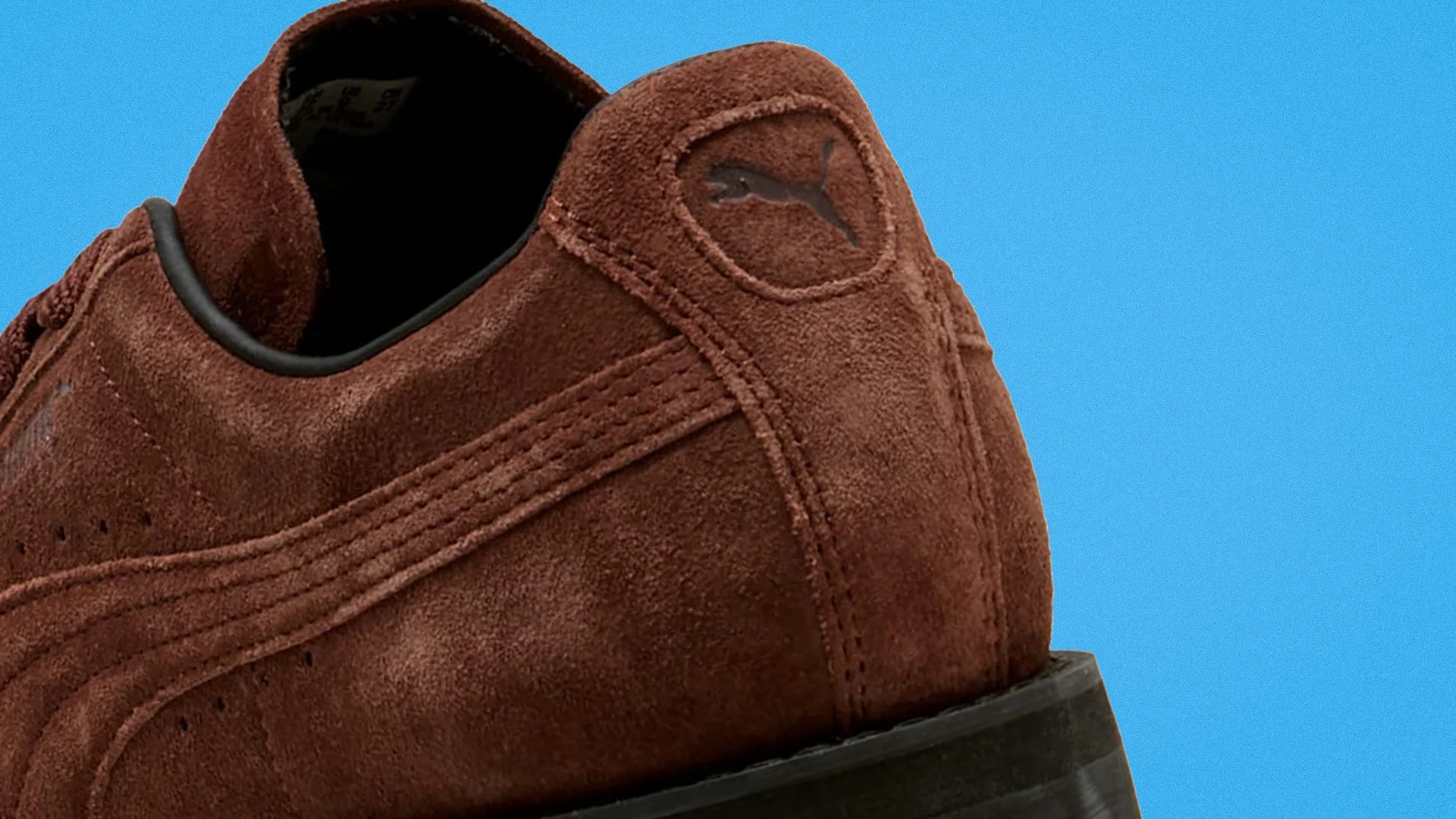Brown suede Puma shoe heel with black sole against a blue background.