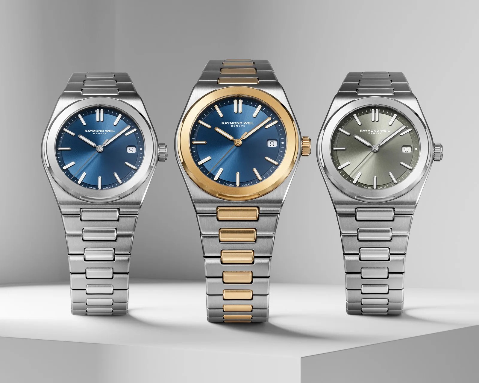 Three Raymond Weil wristwatches with stainless steel bands, two with blue dials and one with a green dial, the center watch has gold accents.